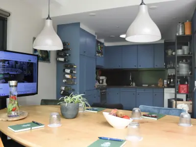 Blauwe keuken met pantry, wijnrek en open kasten, gezien vanaf de vergadertafel met scherm