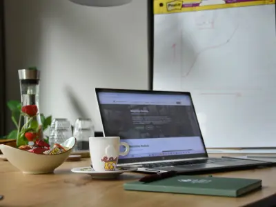 Laptop, espresso en een schaal snacks op de vergadertafel, met op de achtergrond een flip-over met een grafiek
