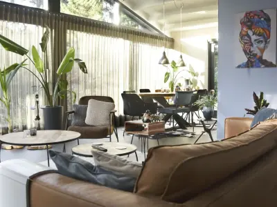 Loungehoek met leren bank, tropische planten en kleurrijk kunstwerk, met de vergadertafel op de achtergrond