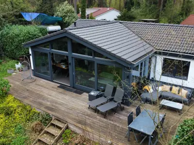 Bovenaanzicht van het ruime houten terras met glazen pui en loungeset aan het boshuis