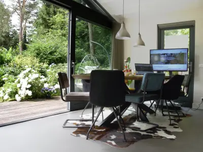 Vergaderruimte met openstaande schuifpui naar het houten terras en bloeiende witte hortensia’s in de bostuin
