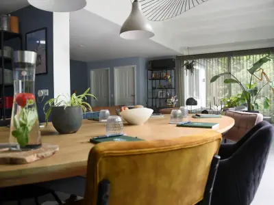 Vergadertafel met karaf aardbeienwater en notitieboekjes tegen een diepblauwe wand, met doorkijk naar de loungehoek vol planten