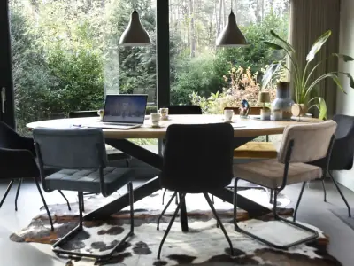 Ovale houten vergadertafel met laptop onder hanglampen, met boszicht door de raampartij