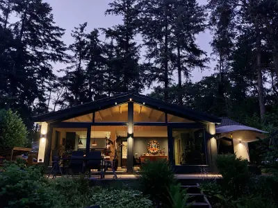 Het boshuis in de avond met verlichte glazen gevel en terras tussen de bomen